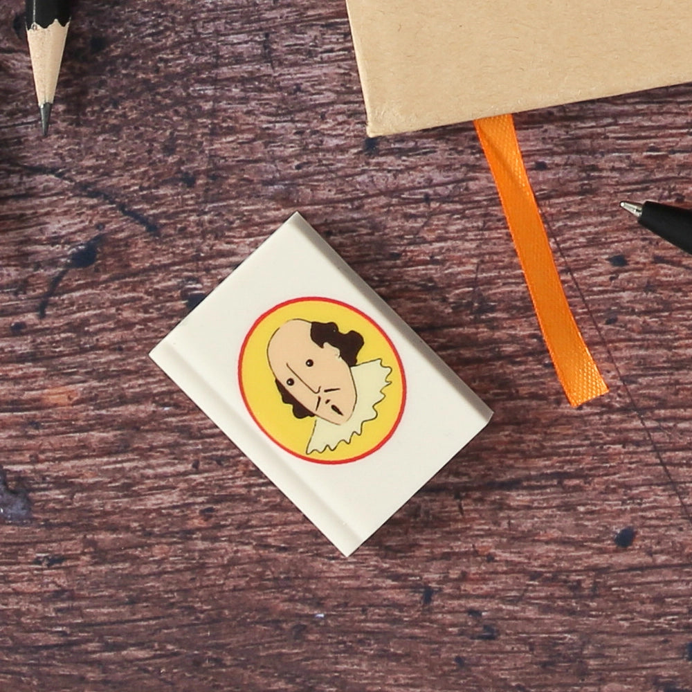 White eraser in the shape of a book printed with a cartoon portrait of Shakespeare on a yellow oval