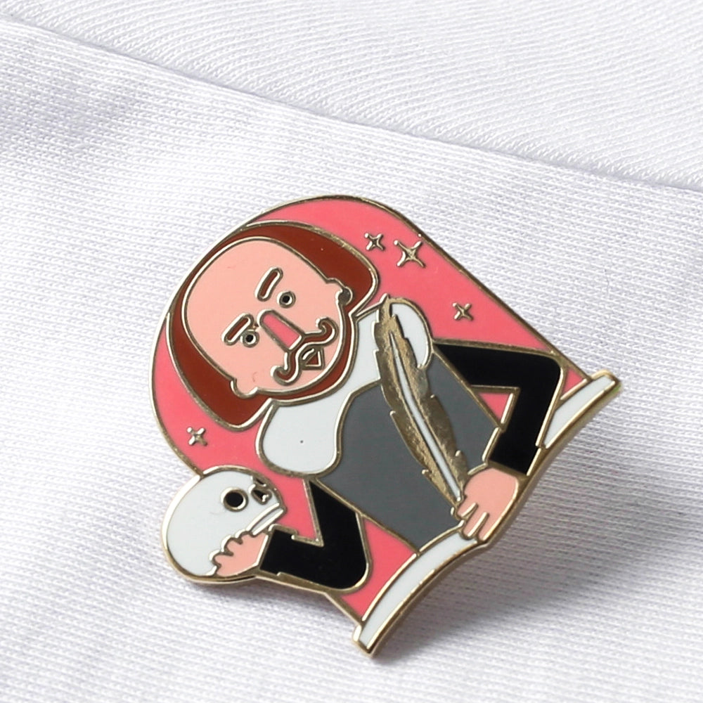 Cartoon metal pin badge of Shakespeare's torso with one hand holding a quill and the other a skull