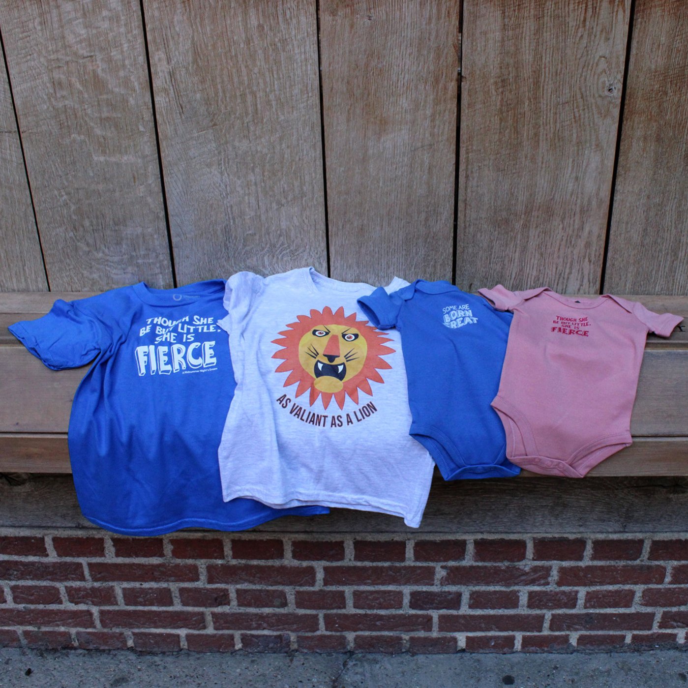 Two childrens t-shirts and two baby grows lying side by side on wooden shelf, from left to right, royal blue, grey, royal blue, pink