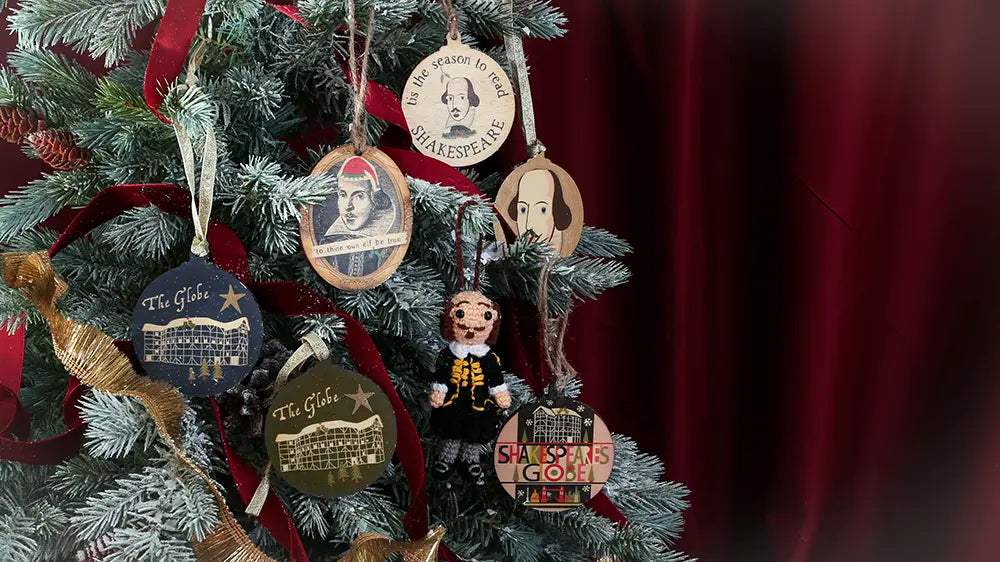 Christmas tree decorated with Shakespeare-themed ornaments, including portraits of William Shakespeare, Globe Theatre decorations, and a small Shakespeare doll, accented with red ribbon.