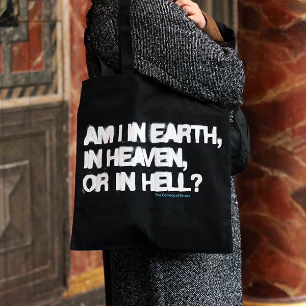 
                  
                    Black cotton bag with black mid-length handles printed with a quote from Shakespeare play, The Comedy of Errors (Am I in earth, in heaven, or in hell?) The letters are printed in bold white san serif capital letters using an expanding dye which gives a sprayed graffiti look.
                  
                