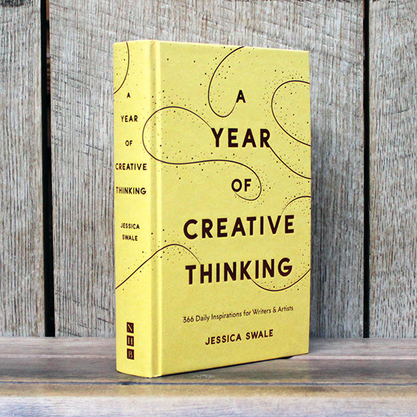 Yellow book titled 'A Year of Creative Thinking' by Jessica Swale on a wooden surface with a wooden background.
