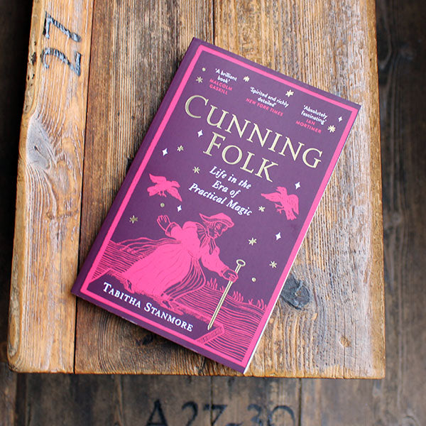 paperback book with a purple and pink cover lying on a wooden bench