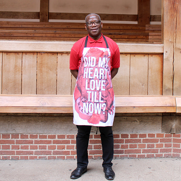 
                  
                    White cotton apron with black ties and red tattoo style graphic hearts with white text overlayed
                  
                