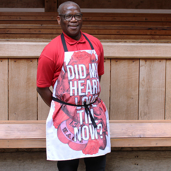 
                  
                    White cotton apron with black ties and red tattoo style graphic hearts with white text overlayed
                  
                