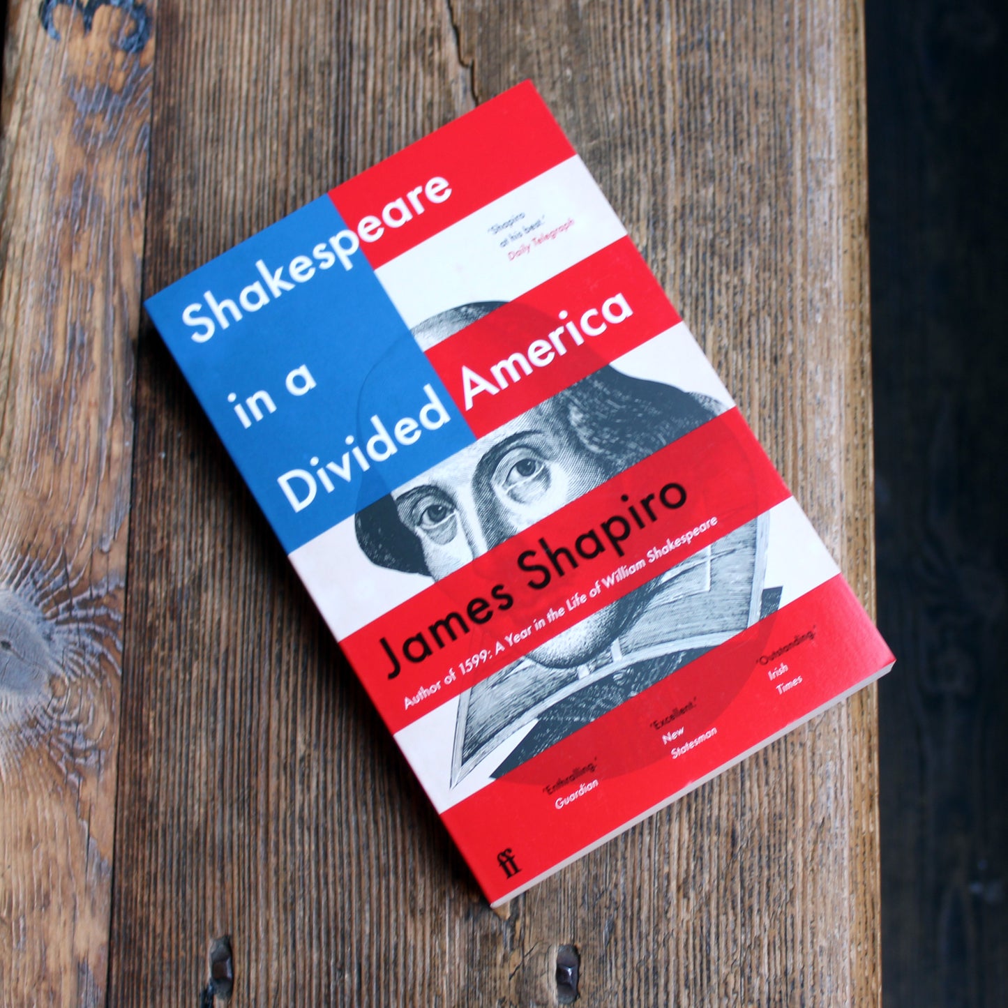 Paperback book with and red, white and blue cover lying on a wooden bench
