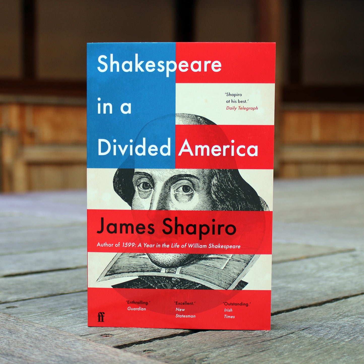 Paperback book with and red, white and blue cover standing on a wooden stage