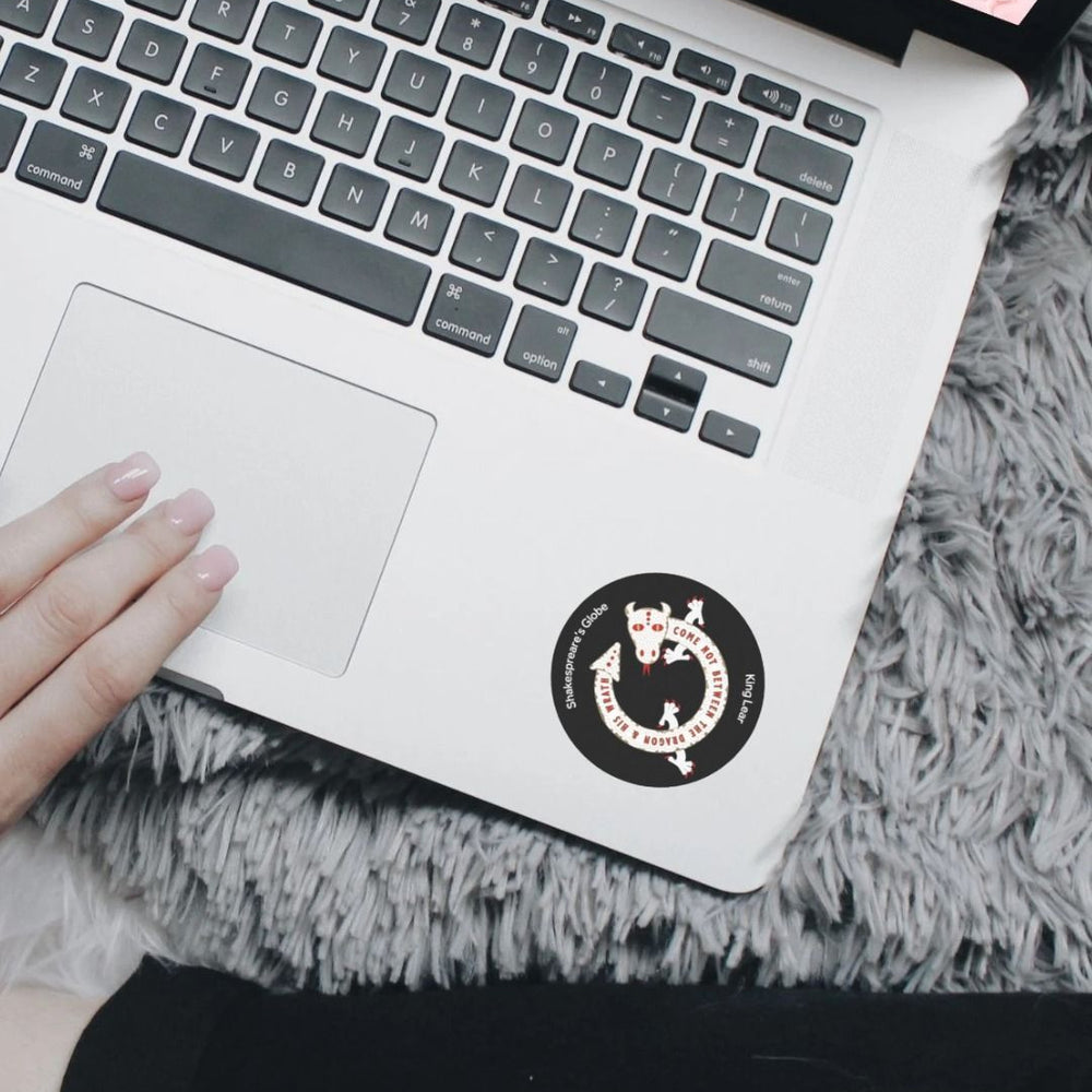 Black circular sticker with white graphic of a dragon, stuck on a silver laptop