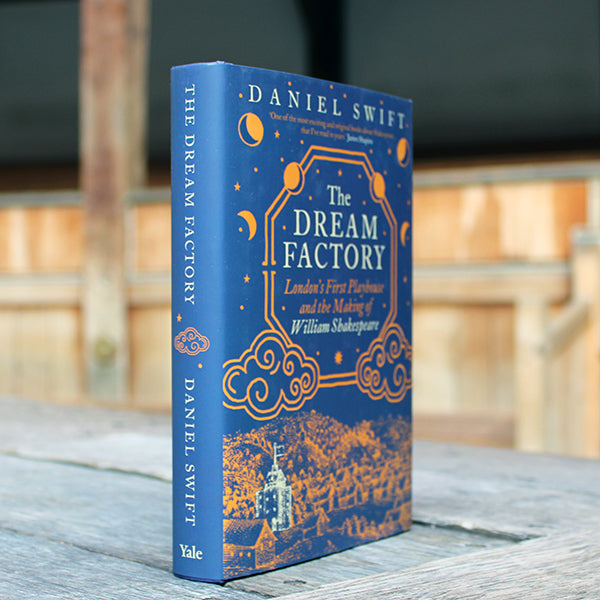 Navy blue hardback book with gold and white etchings and writing, sitting on wooden stage, book at an angle showing spine