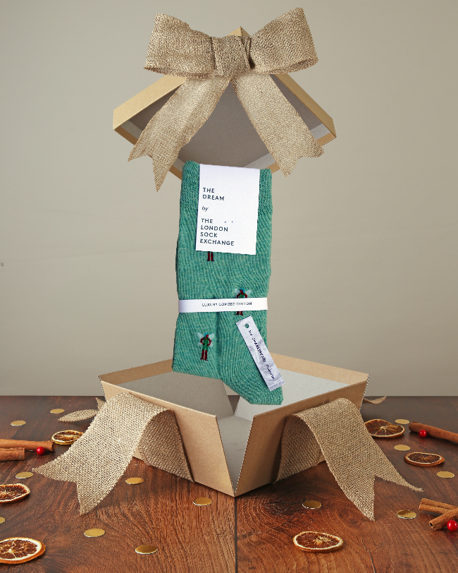 Teal printed cotton socks popping out of kraft box with bow on wood base with Christmas decor