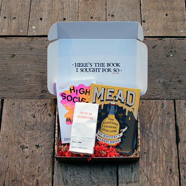 Brown kraft gift box with white interior, featuring black block text and with two books and one paper bag of poetry prescription pills sitting inside