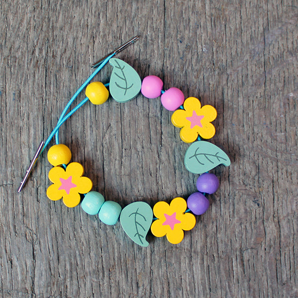 Wooden bracelet kit with green leaves, yellow flowers, and yellow, purple, pink, and teal balls on teal stretch string