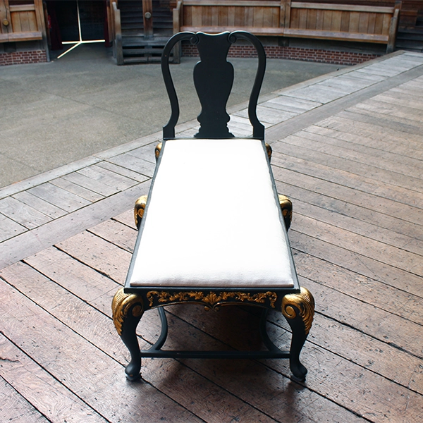 
                      
                        Matt grey with gold leaf detailing chaise long with white cheesecloth upholstery, sitting on wood panel stage
                      
                    