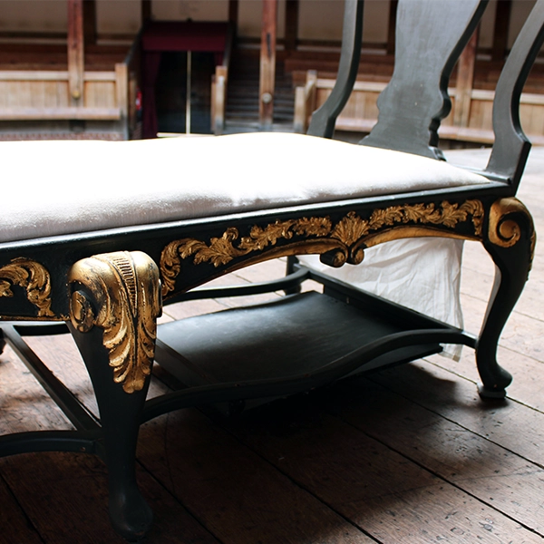 
                      
                        Matt grey with gold leaf detailing chaise long with white cheesecloth upholstery, sitting on wood panel stage
                      
                    