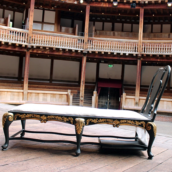 
                      
                        Matt grey with gold leaf detailing chaise long with white cheesecloth upholstery, sitting on wood panel stage
                      
                    