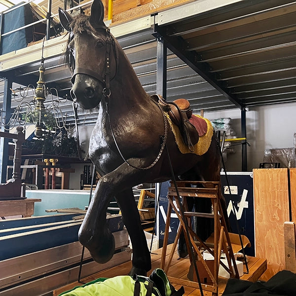 Brown fibreglass life-sized horse with saddle and reigns, sitting in warehouse