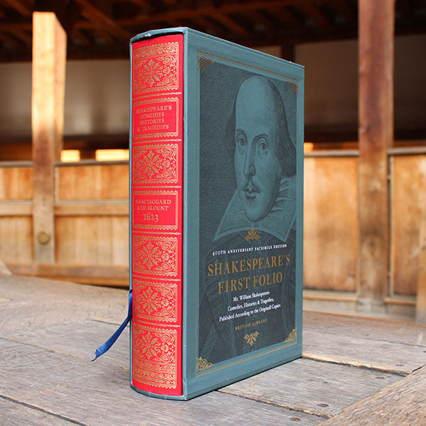 Shakespeare's First Folio book with red and blue binding on a wooden surface