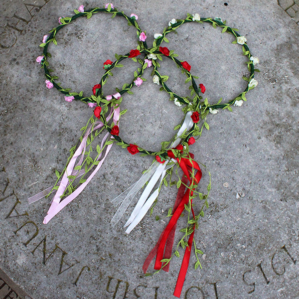 Faux flower and greenery flower crowns, one each of red flower, white flower, pink flower, on stone surface