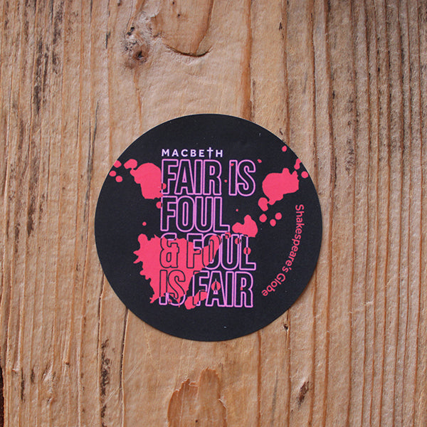 Black circular sticker with pink outlined graphic text across it, covered in bold red blood splatter design, stuck on wood