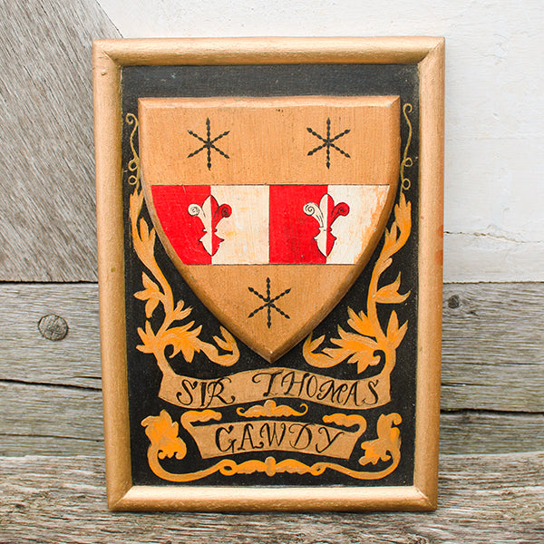 Wooden shield with coat of arms and 'Sir Thomas Gawdy' inscription on a wooden background