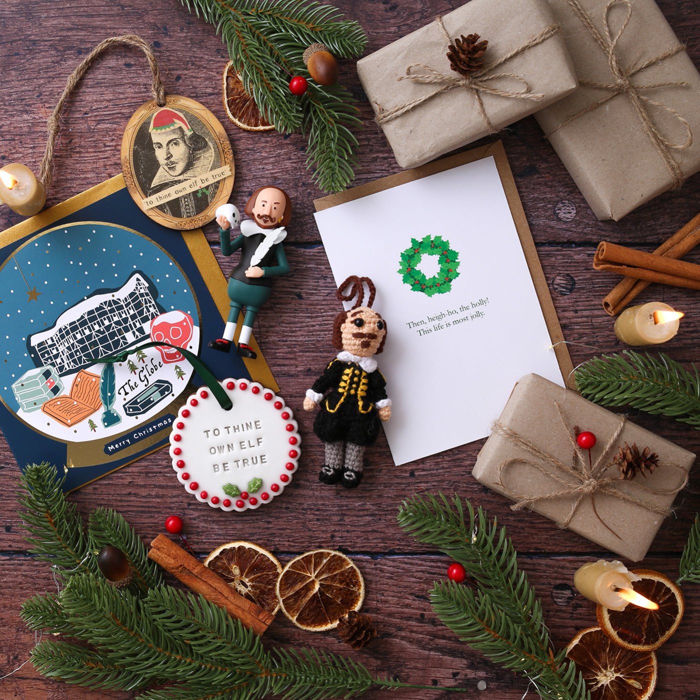 Selection of Christmas decorations, Christmas cards, dried orange slices, cinnamon sticks, greenery, and wrapped brown packaged on wood panel background