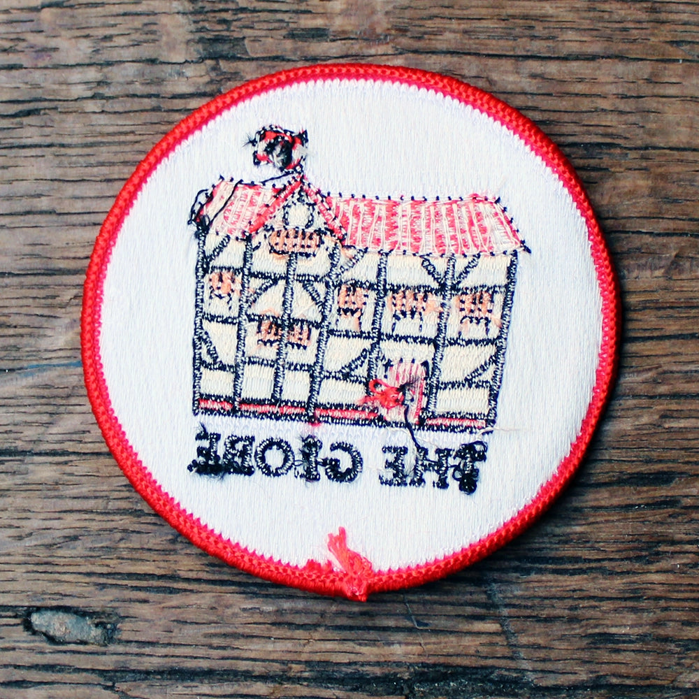 
                      
                        White circular embroidered badge with red border, featuring black, beige and red cartoon Globe in the centre, from reverse side
                      
                    