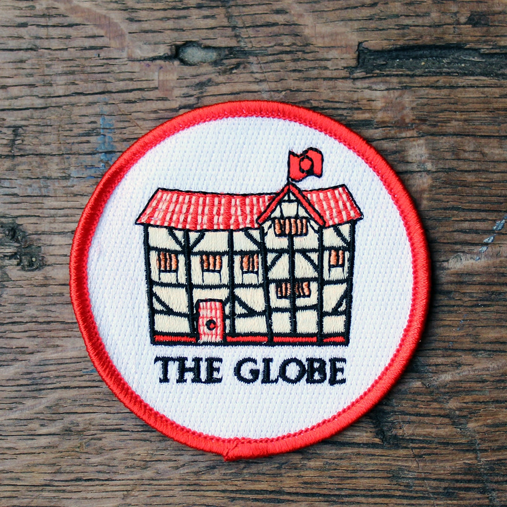 White circular embroidered badge with red border, featuring black, beige and red cartoon Globe in the centre