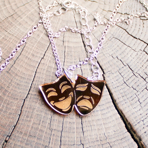 Necklace with gold coloured theatre mask pendants on a wooden surface