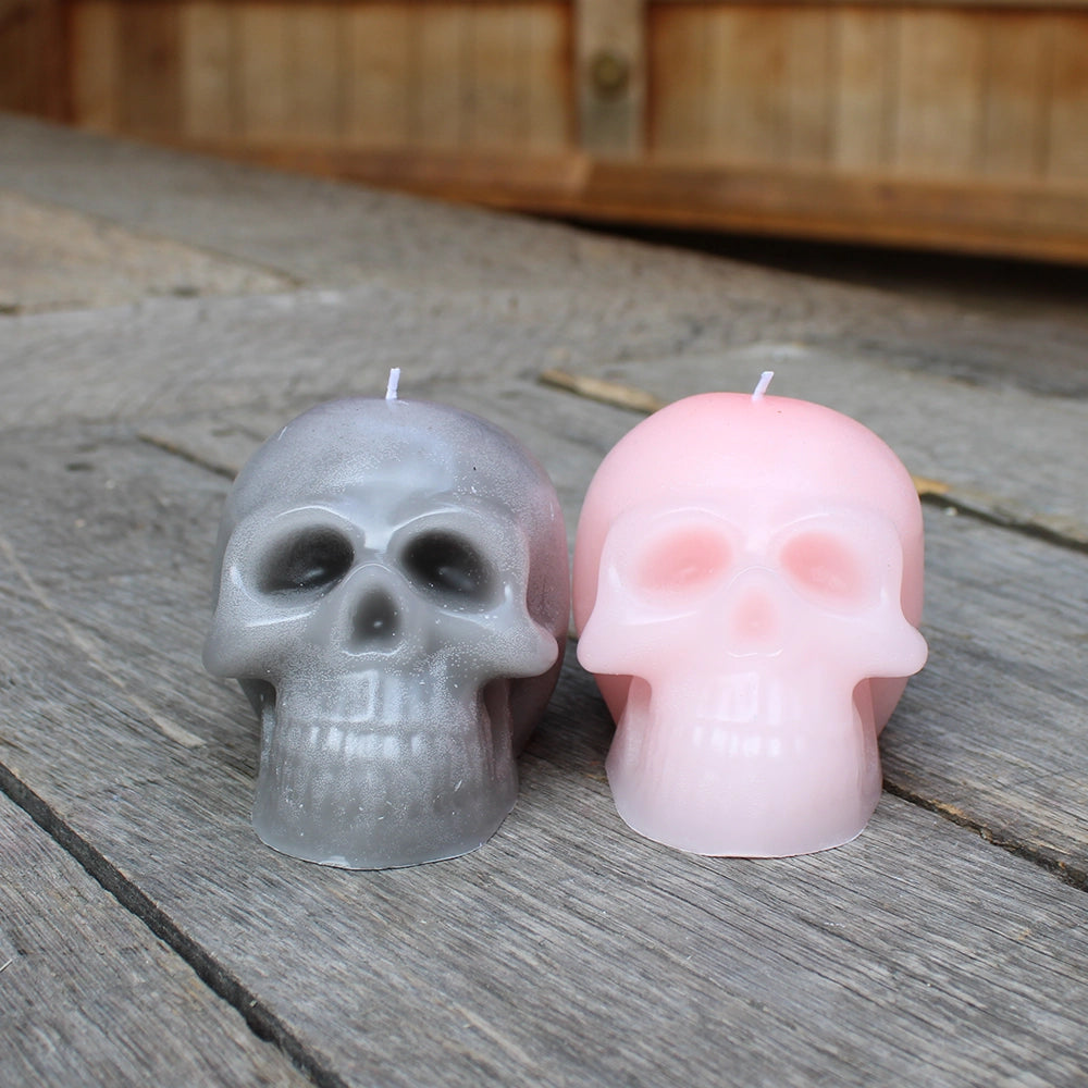 Grey and pale pink skull candles sitting side by side on wooden stage