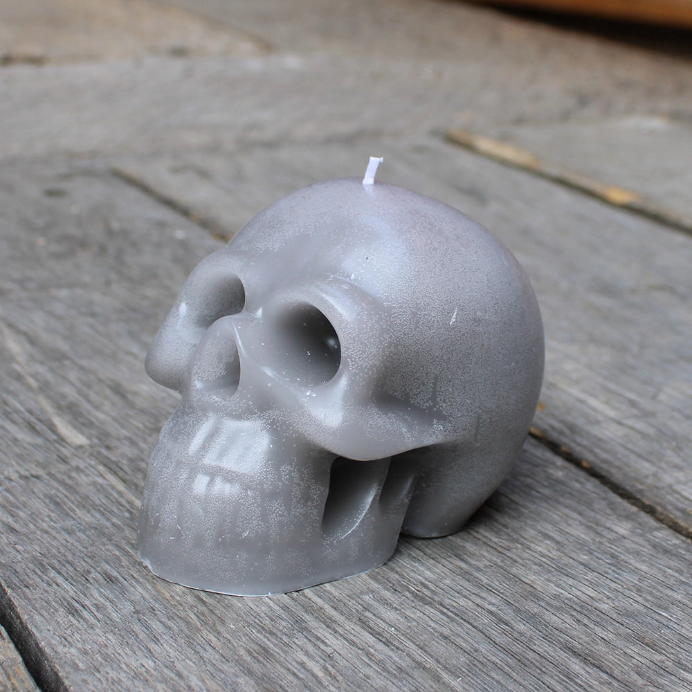 
                      
                        Pale black/grey skull candle with white wick, sitting on wooden stage
                      
                    