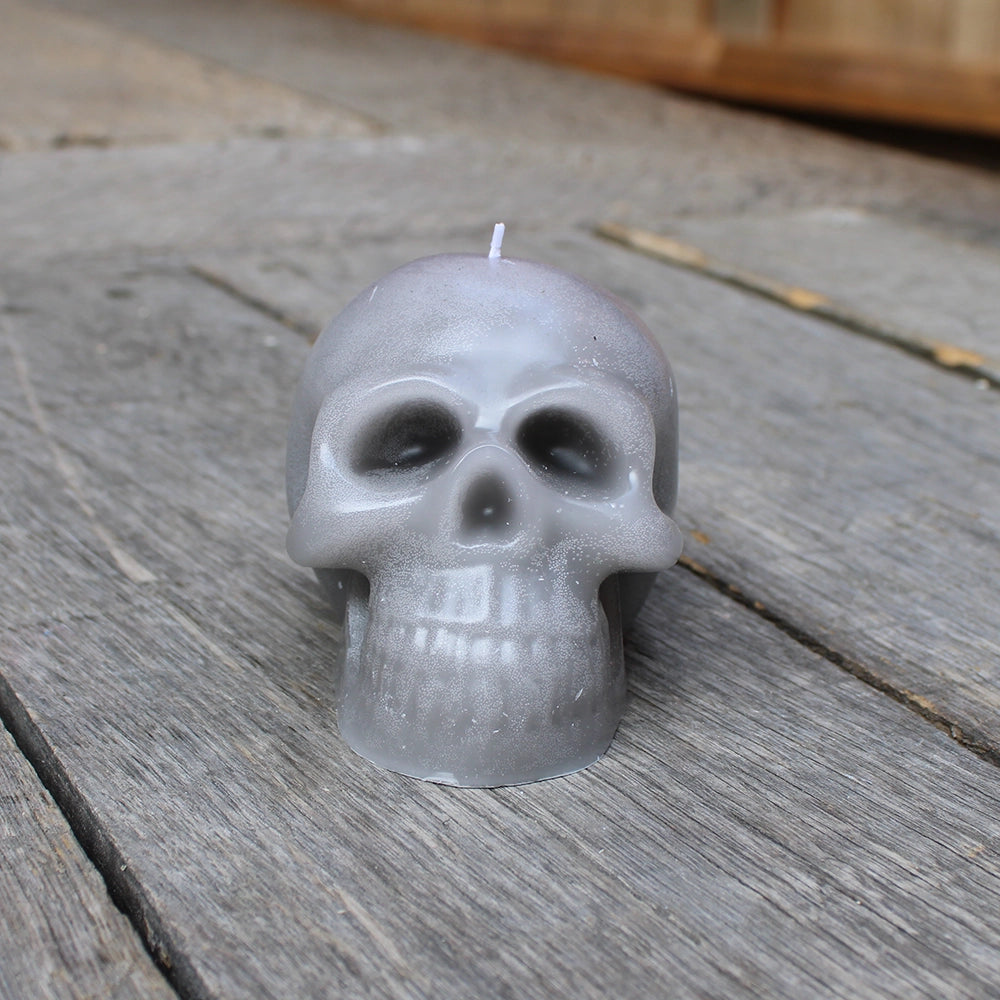 
                      
                        Pale black/grey skull candle with white wick, sitting on wooden stage
                      
                    