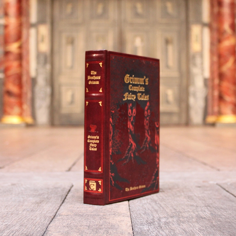 Red leatherbound book with gold script writing and etched forest motif