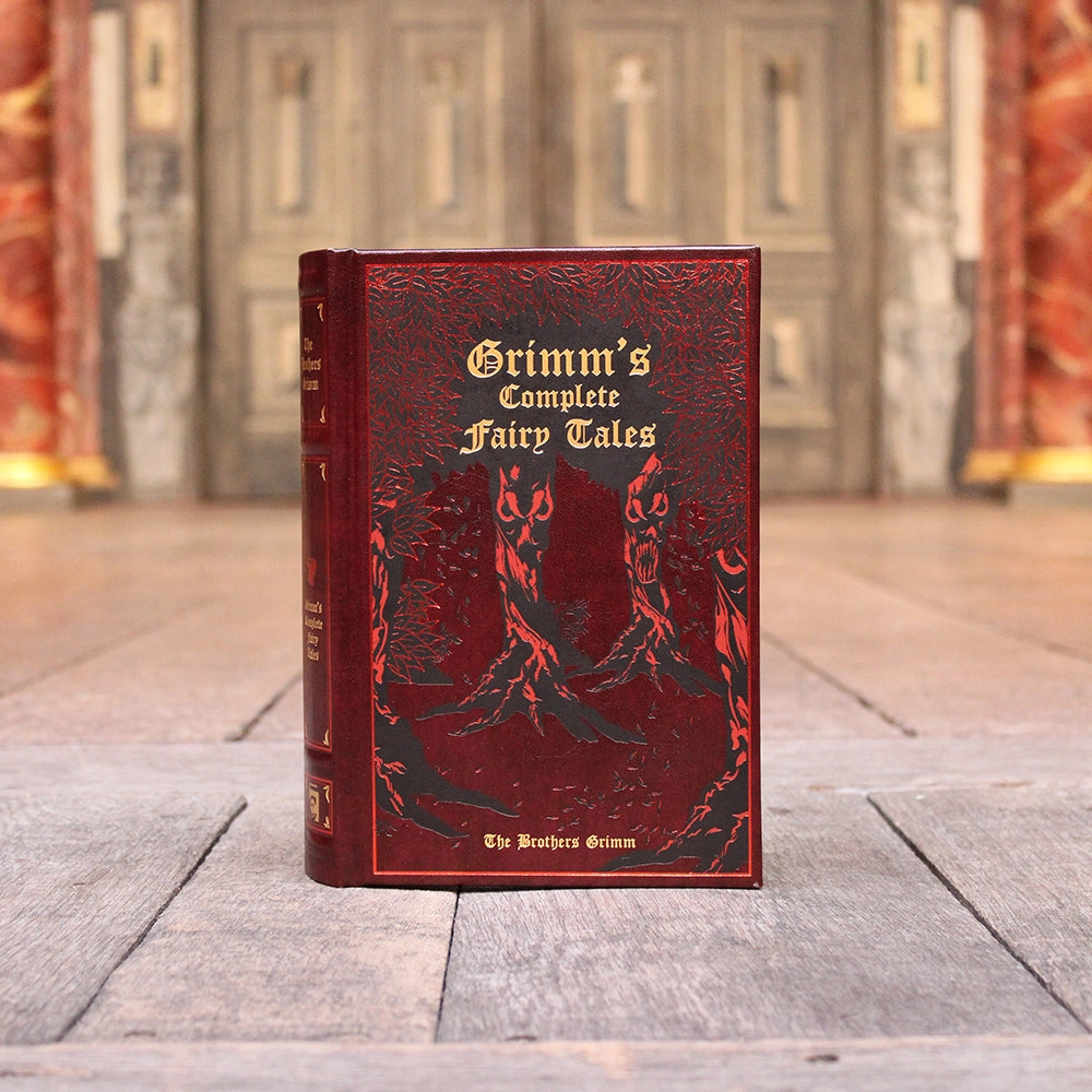 Red leatherbound book with gold script writing and etched forest motif