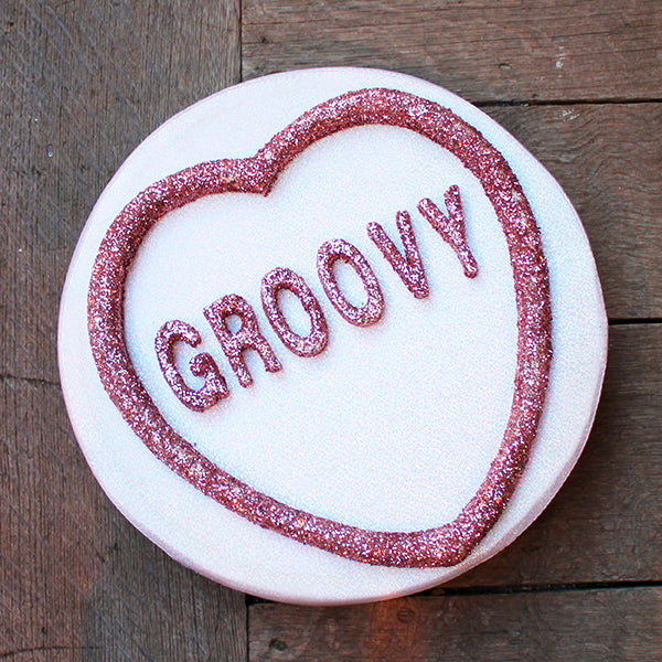 Round white prop with pink 'Groovy' text on a wooden surface