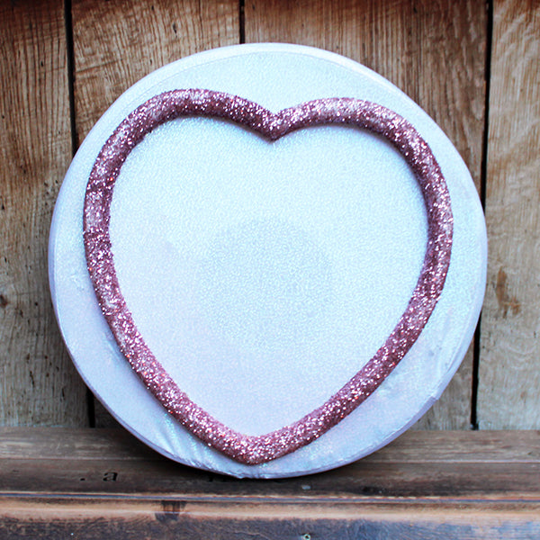 Decorative item with a heart-shaped pink glitter border on a wooden surface