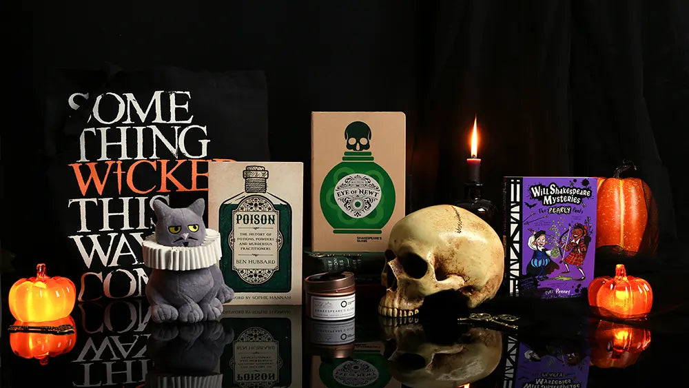 Halloween display featuring a ‘Something Wicked This Way Comes’ tote bag, a skull, glowing pumpkins, a black cat figurine, a lit candle, spooky bottles, and a William Shakespeare Mysteries book against a dark background
