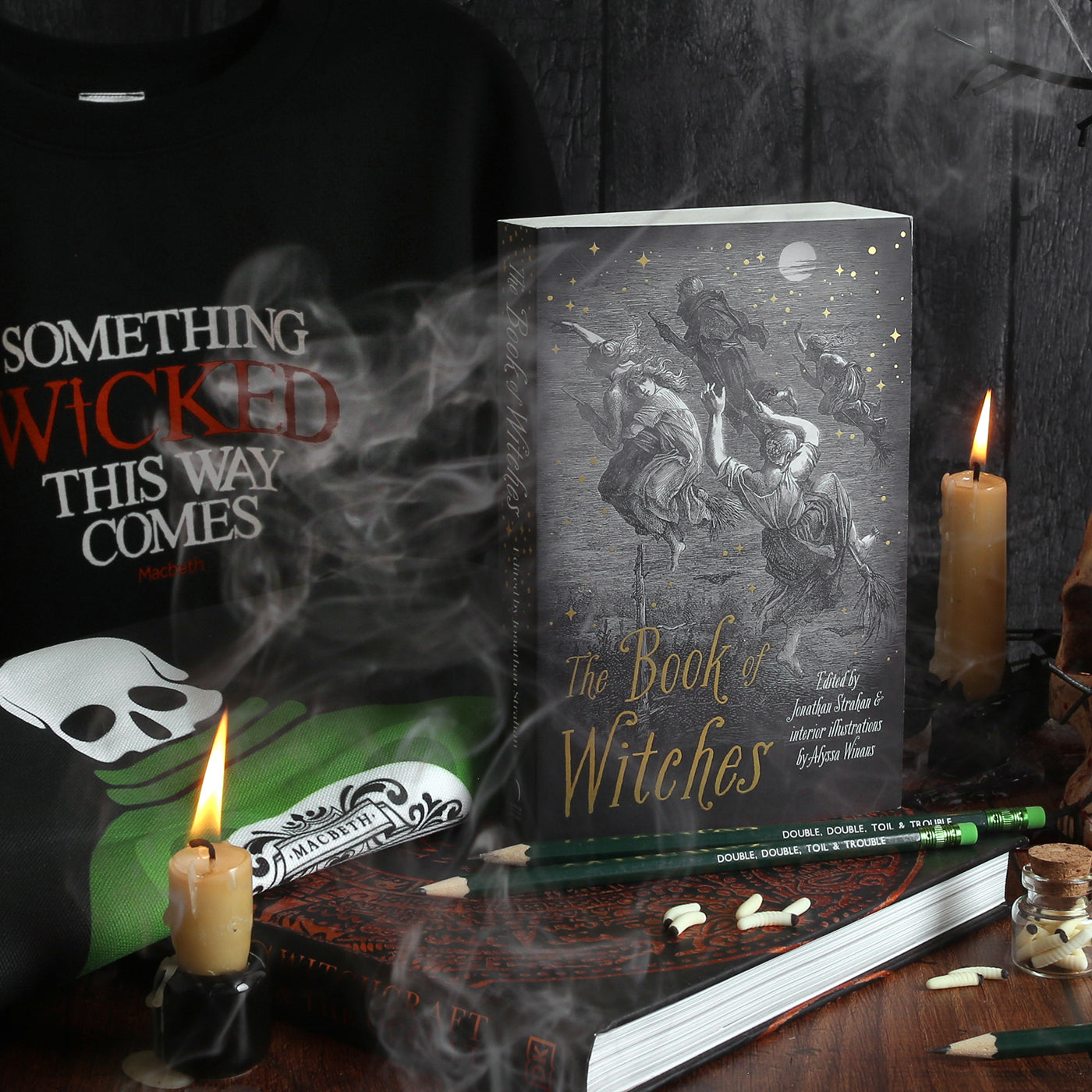 Black moody image of 2 lit candles, smoke, black paperback book, black hardback book, poison tote bag and wicked sweatshirt