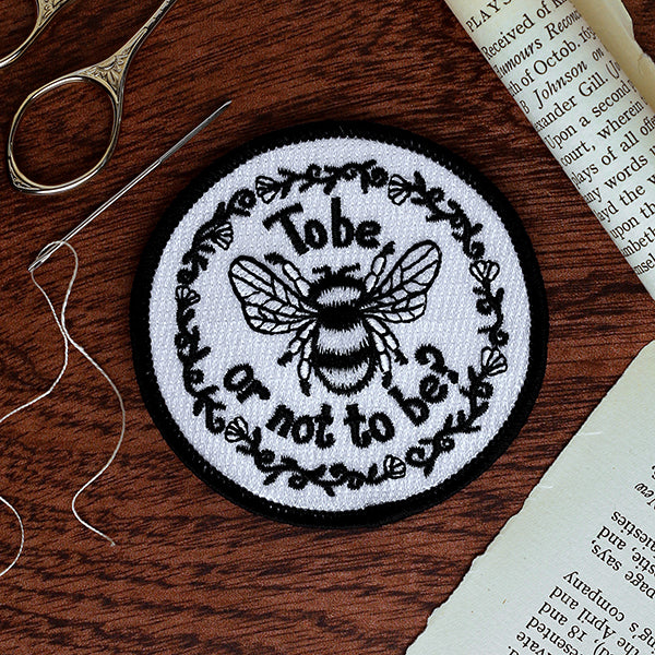 Embroidered patch with bee design and text on a wooden surface with sewing tools.