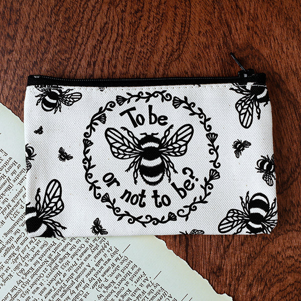 White purse with black bee design and text 'To be or not to be?' on a wooden surface.