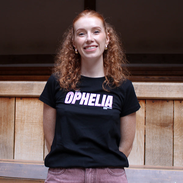 Person wearing a black t-shirt with 'OPHELIA' printed on it, standing against a wooden wall.