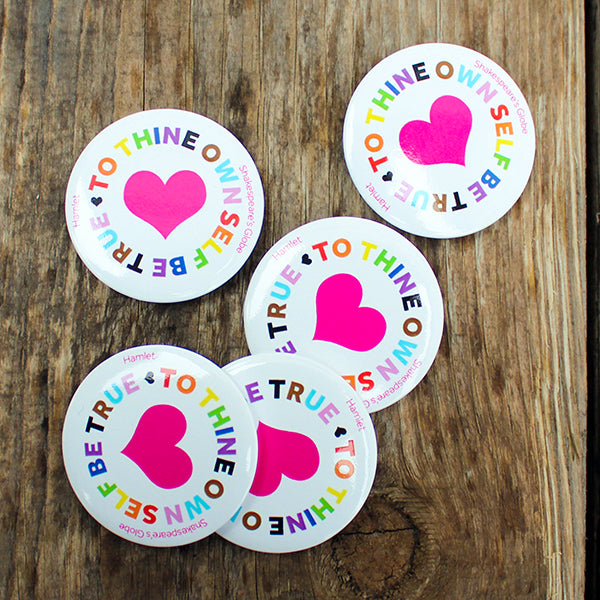 Five round badges with pink hearts and colourful text on a wooden surface