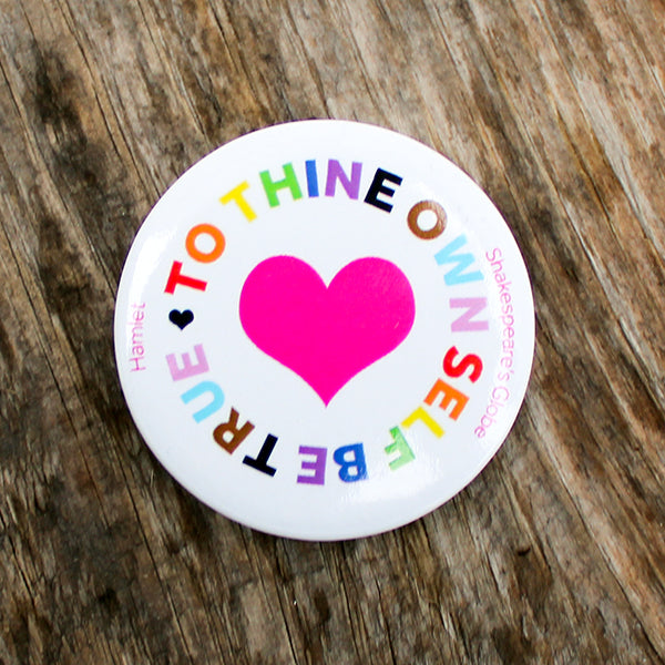 Round badge with a pink heart and colorful text on a wooden surface