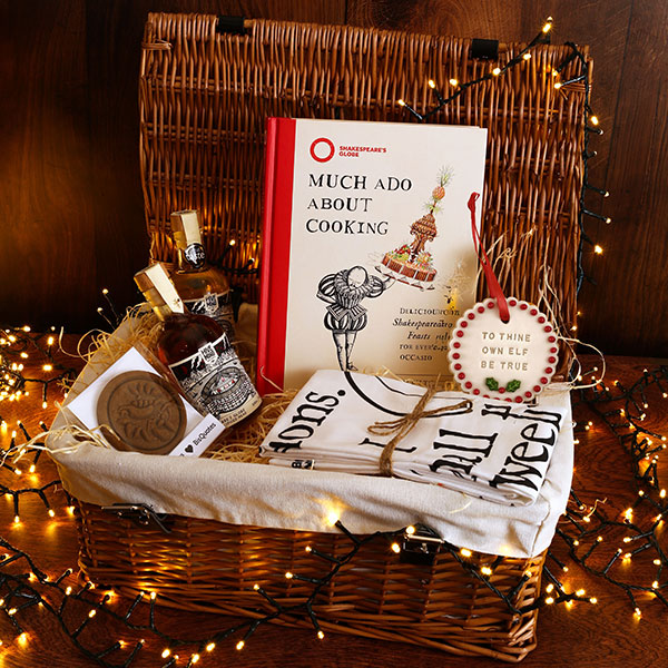 Gift basket with books, a bottle of mead, and decorative items on a wooden surface with string lights.