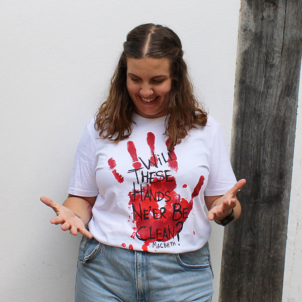 Woman with shoulder length brown curly hair in light blue jeans and white graphic t-shirt with bloody hand print across it