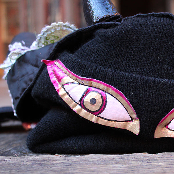 Black knitted hat with a decorative eye patch on a wooden surface