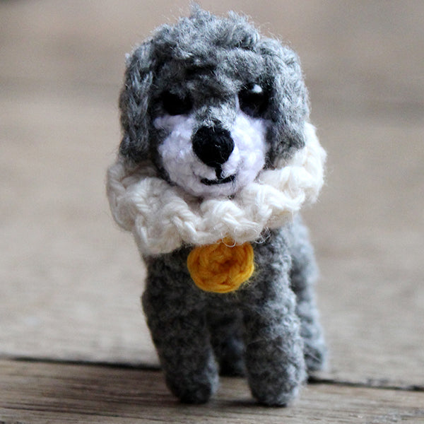 crocheted dog made from grey yarn with a white muzzle and black eyes. The dog wears a white ruff collar with a yellow tag