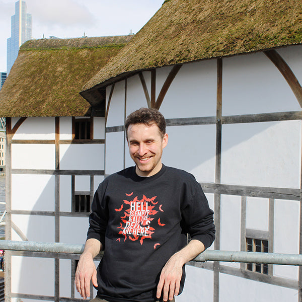 Black polycotton sweatshirt with red bats graphic in centre, overlayed with white text, sweatshirt is worn by a male who is standing in front of the Globe Theatre