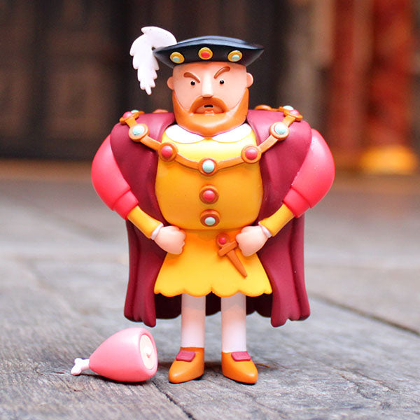 Toy figure of a character in regal attire with a red cape and yellow outfit on a wooden surface.