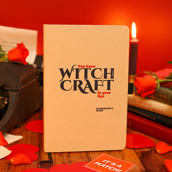 Notebook with 'You have WITCH CRAFT in your lips' text on a wooden surface with a red background
