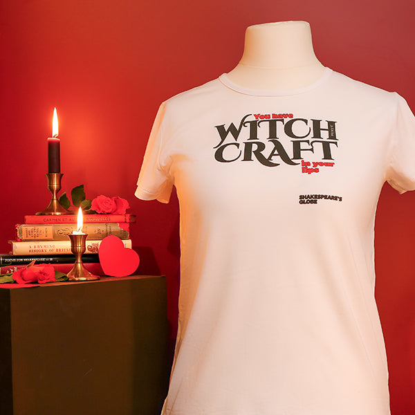 White t-shirt with 'Witch Craft' text on a mannequin against a red background with candles and books.